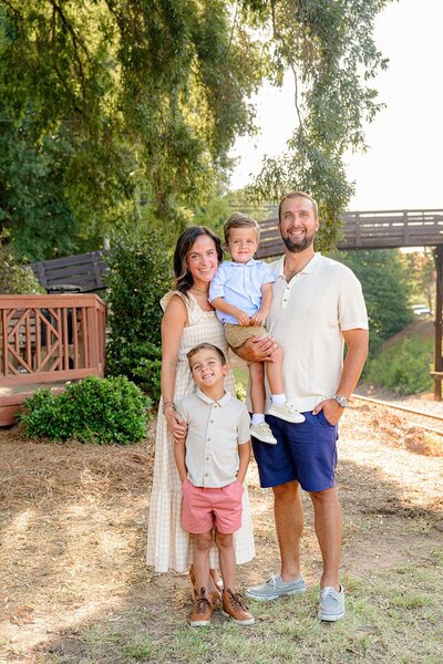 family of four wearing neutral colors posed in front of the waxhaw bridge in downtown
