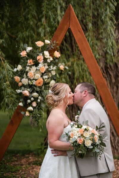bride and groom kissing under the arch at barnwood events in madison, winconsin.
