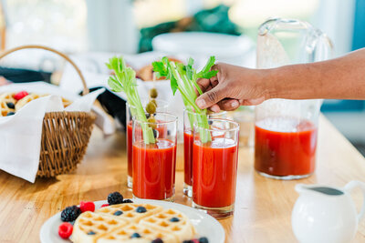 Hand placing celery in bloody marry and waffles on the table
