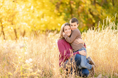 Mother in pink sweater hugging her young son wearing a brown shirt and blue jeans in a field of yellow grass by Chicago Family Photographer Kristen Hazelton