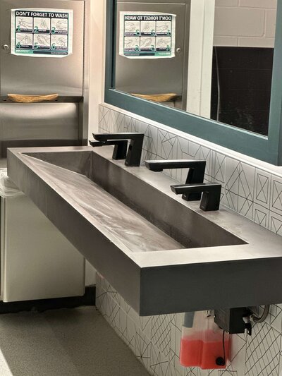 Concrete ramp sink with two faucets that meets ADA sink requirements for performing arts center bathroom in Minnesota