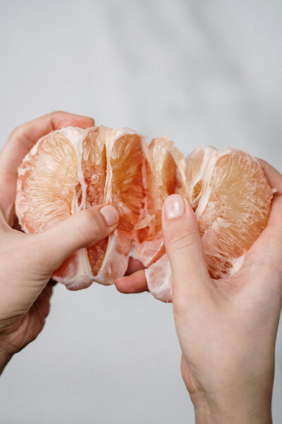A person holding a half grapefruit, showcasing its bright pink flesh and textured rind.