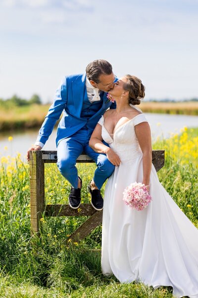 Romantisch moment tussen bruid en bruidegom tijdens hun bruiloft, vastgelegd met hulp van een weddingplanner; zij met boeket, hij zittend op een hek