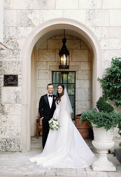 Groom and bride stand in front of an arch.