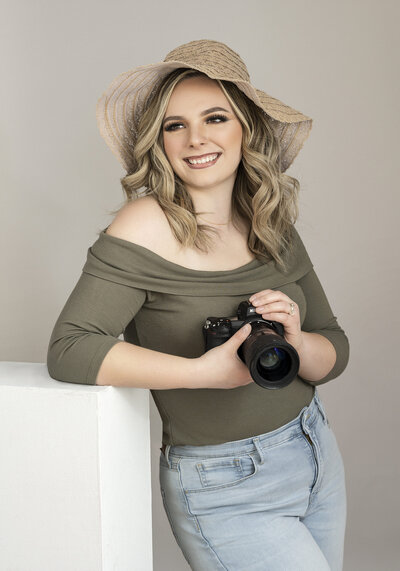 The owner of Kara Reese Photography, Kara Krause, pictured holding her camera for a headshot.