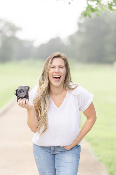 Brittany, associate NoVa photographer who takes on family, maternity, cake smash, newborn, and senior sessions, holding a camera laughing
