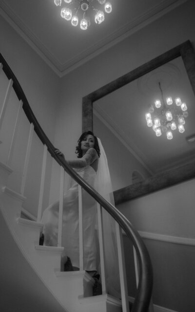 Black and white image of a bride gracefully walking up the stairs, capturing a timeless and elegant moment filled with anticipation and bridal beauty