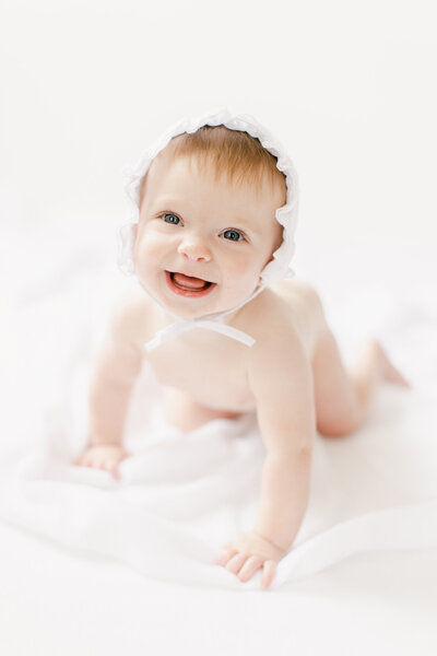 six month old baby in bonnet in all white studio.