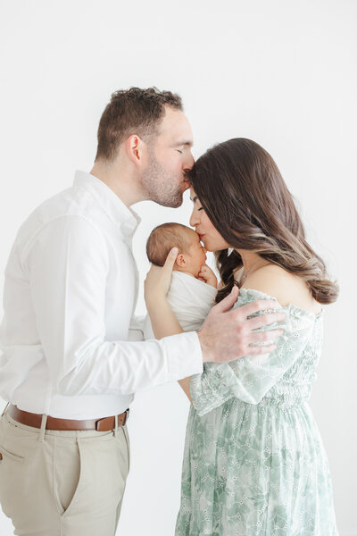 New parents kiss their newborn babies forehead and embrace during newborn portrait session