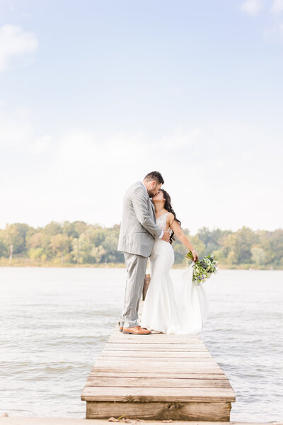 bride and groom kissing on a dock overlooking the river