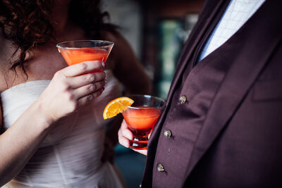 Two people standing close holding cocktails.