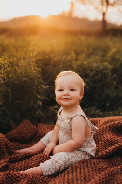 Golden hour photo of toddler sitting on blanket in field of grass