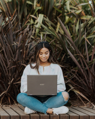 Girl sitting outside in front of plants, while working on her laptop