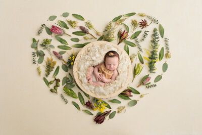 newborn in a bowl surrounded by flowers in the shape of a heart