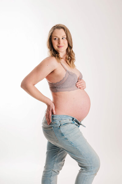 A pregnant woman looking off to the side in blue jeans and short top