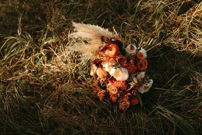 Rust colored bouquet with pampas grass laying on ground at sunset