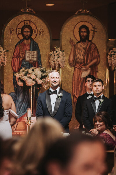 Smiling groom watching bride enter and walk toward him in classic church setting - professional editing sample