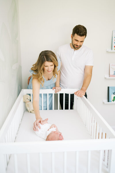Couple looks into white crib at sleeping baby girl during newborn photo session in Raleigh