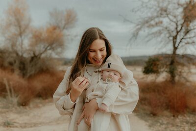 A woman holding a baby on a dirt road.
