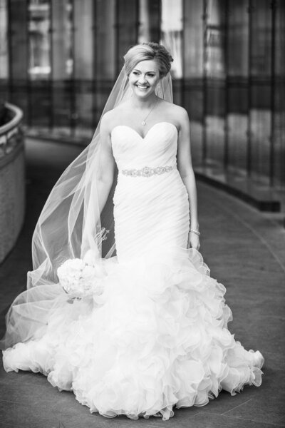 An editorial photo of a bride is walking while holding her bouquet down with her right hand and not looking at the camera.