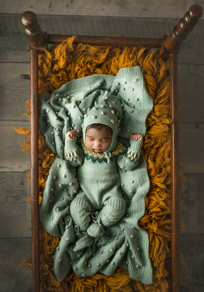 newborn in crib at portrait session in handmade knits in clarkston michigan studio