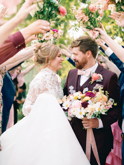 Bride and Groom smiling at each other with colorful flowers at garden party wedding