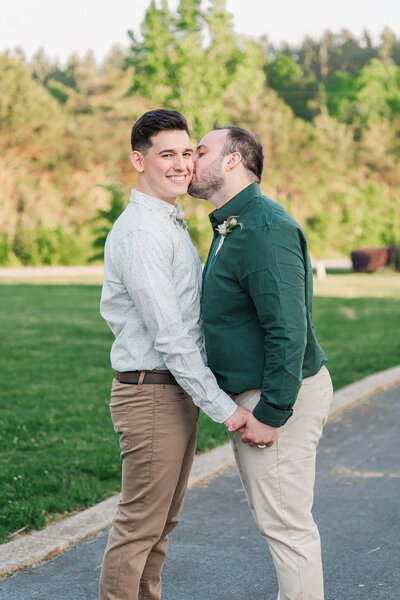 A loving same sex couple sharing a kiss on the cheek at sunset at Highrock Farms while enjoying their Raleigh wedding photography session with JoLynn Photography