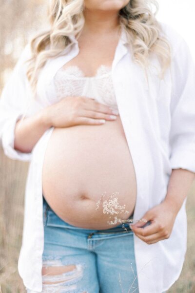 Woman in maternity gown stands in field of grass holding pregnant belly.