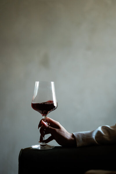 Hand holding a wine glass resting on the arm of a chair against a solid background