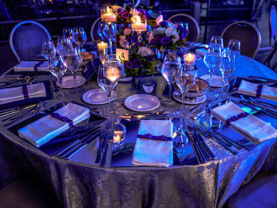 Round table with table napkins, utensils, glasses , lighted candles and a flower centerpiece