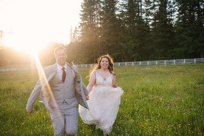 Bride and groom running in a field at sunset