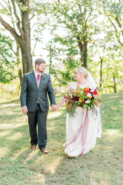 Couple walking with loose fall bouquet at their family estate wedding