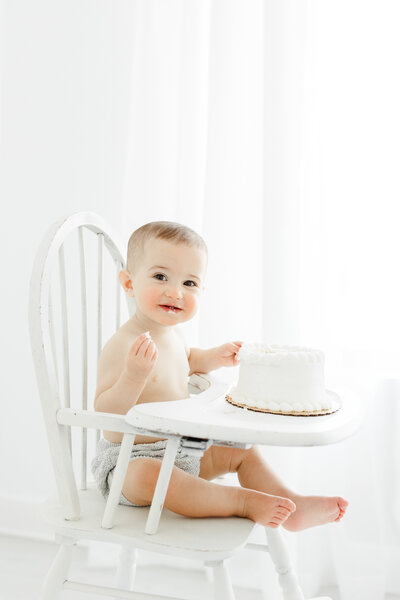 One year old baby boy sits in high chair ready to smash his first birthday cake during portrait session