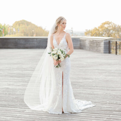 a full length photo of a bride holding her bouquet on the deck of the NAC taken by Ottawa wedding photographer JEMMAN Photography
