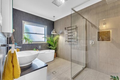 Modern bathroom with a freestanding bathtub, walk-in shower, indoor plants, and neutral floor-to-ceiling tiles.