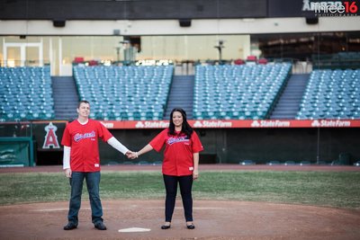 Engaged couple hold hands and pose for photos at home plate inside Angel Stadium