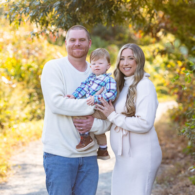 photo of a family of three and pregnant mother standing outside in the fall taken by new jersey family photographer ally kimpton 