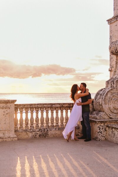 man and woman kissing on balcony in front of ocean