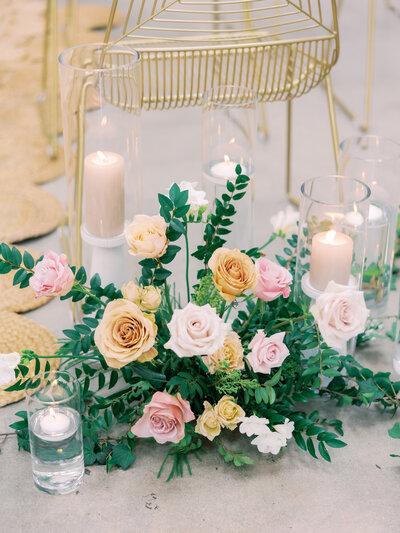 This bouquet golds golden, pink and white roses along with greenery in the center of a group of candles.