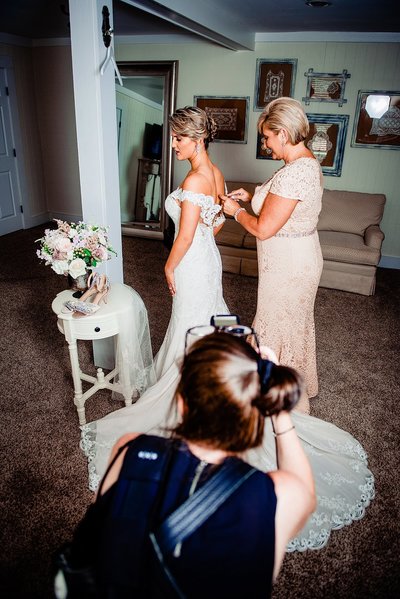 Behind the scenes photo of a photographer taking getting ready photos of mom zipping her daughter into her wedding dress.