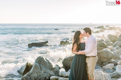 Bride to be sits on her Groom's lap as they pose while sitting on rocks with their initials at the Harbor Point Conservation Park in Dana Point