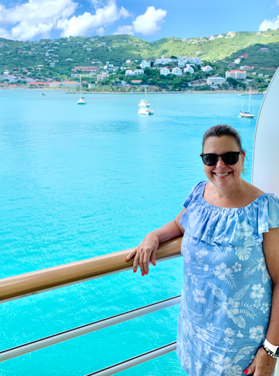 Woman in blue dress on verandah of Disney Cruise ship overlooking tropical harbour