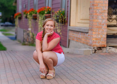 high school senior girl squatting on sidewalk downtown