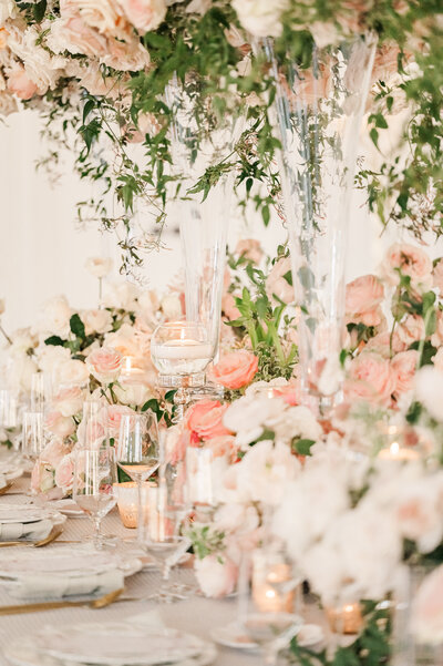 A gorgeous floral array of pink, white, and pastel florals on top of a warm green table cloth, fine china, and warm lighting at Donovan Manor by destination wedding photographer, JoLynn Photography