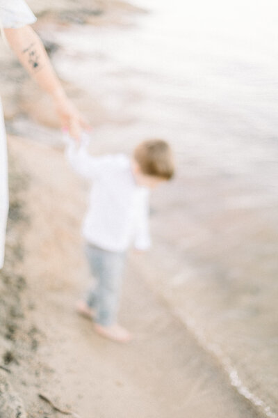 Blurred image of little boy holding his mothers hand by the water taken by Family Photographer Sacramento Kelsey Krall Photography