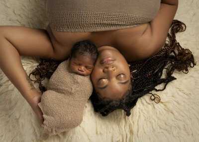 Peacefully sleeping newborn baby boy securely wrapped in a soft blanket, snuggles next to his African American mother with beautiful braids. Captured in soft neutral tones by Charlotte Family Photographer Insley Photo