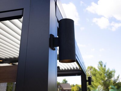Black accent light side-mounted to the outside of a black StruXure pergola. 