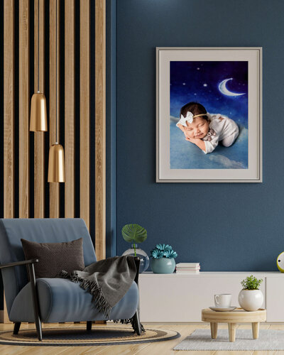 A cozy modern living room with a blue accent wall, armchair, and side table set for tea features a framed photo by a Jacksonville newborn photographer—showing a smiling baby lying on a cloud under a crescent moon.