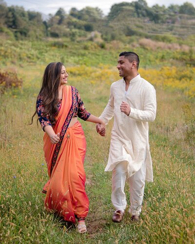 Indian couple laughing and smiling at each other holding hands running in a field