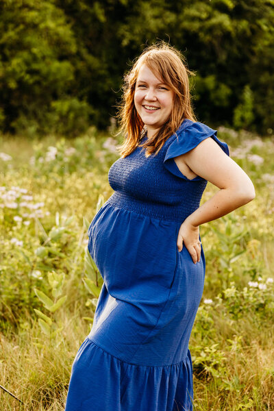 expecting mama in blue dress laughing in a wildflower field during maternity session